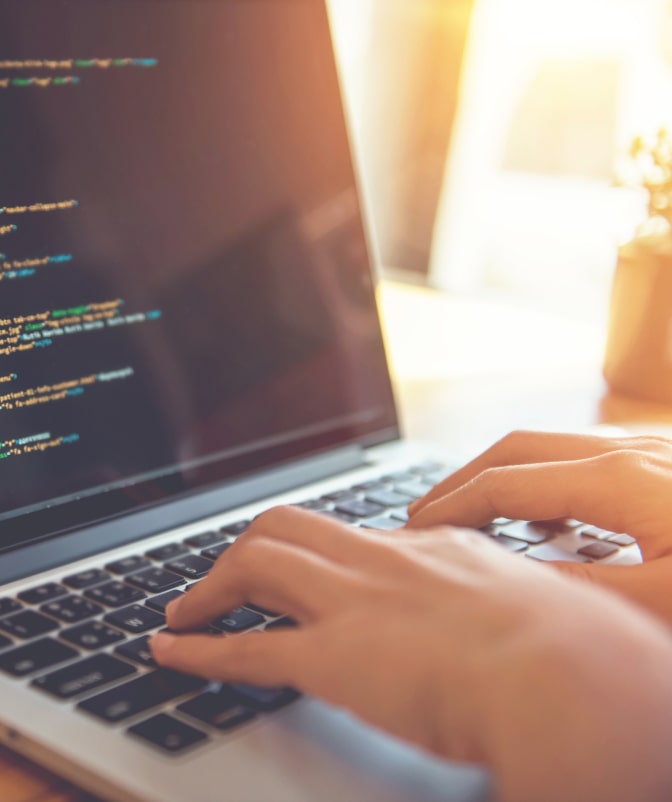 Close-up of hands typing code on a laptop screen, with warm sunlight shining through a window