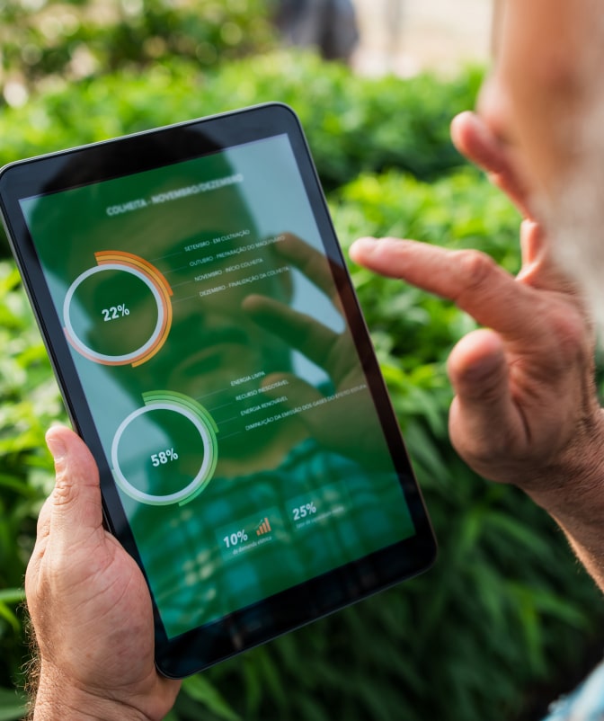 Close-up of a person analyzing circular charts on a tablet screen, reflecting green plants in the background