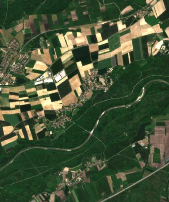 High-resolution satellite image showing patchwork farmland, a winding river, and surrounding green forest areas