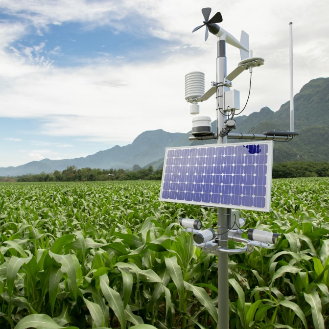 A high-tech weather station powered by solar energy, monitoring environmental conditions in a cornfield with mountains in the background