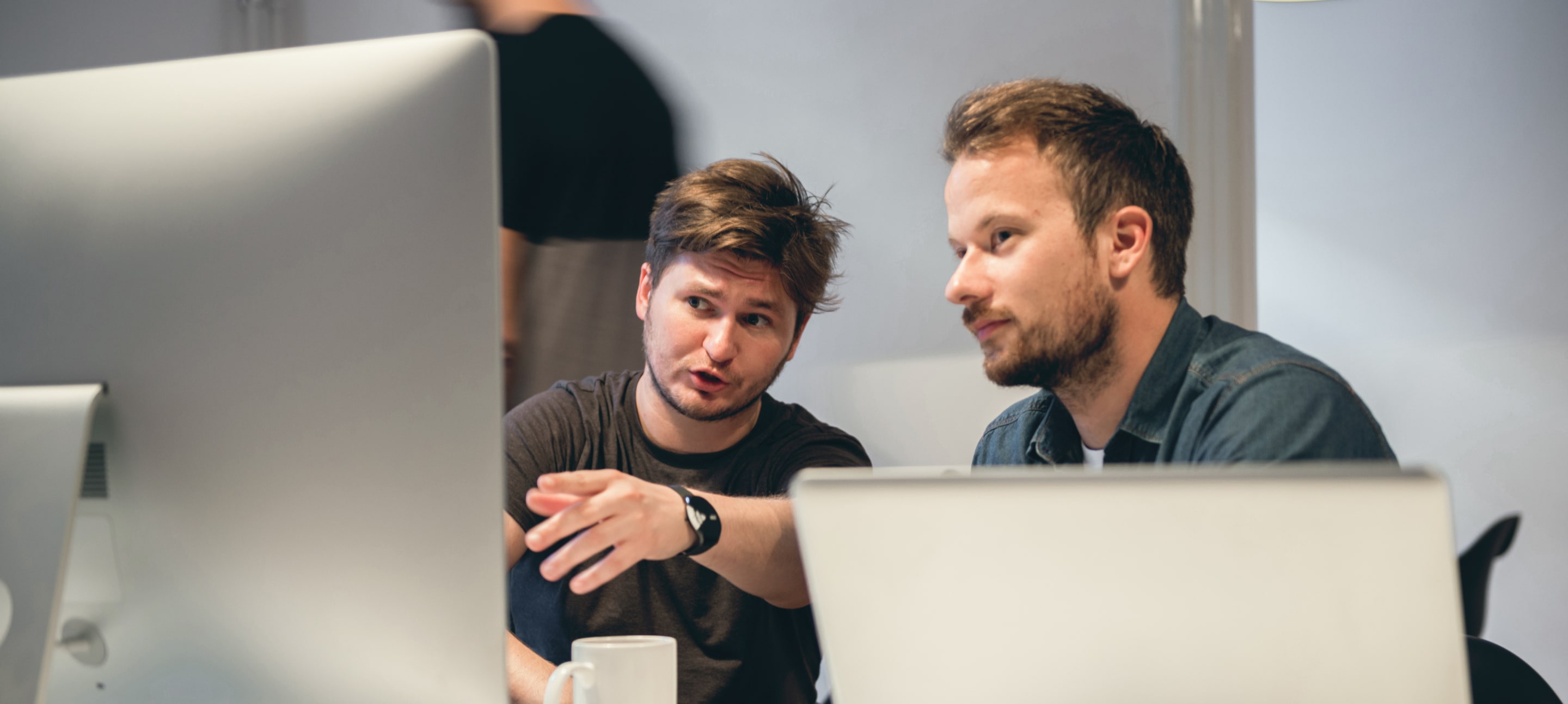 Two colleagues discussing a project in front of a computer screen, working together in a modern office setting