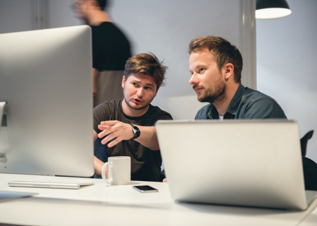 Two colleagues discussing a project in front of a computer screen, working together in a modern office setting