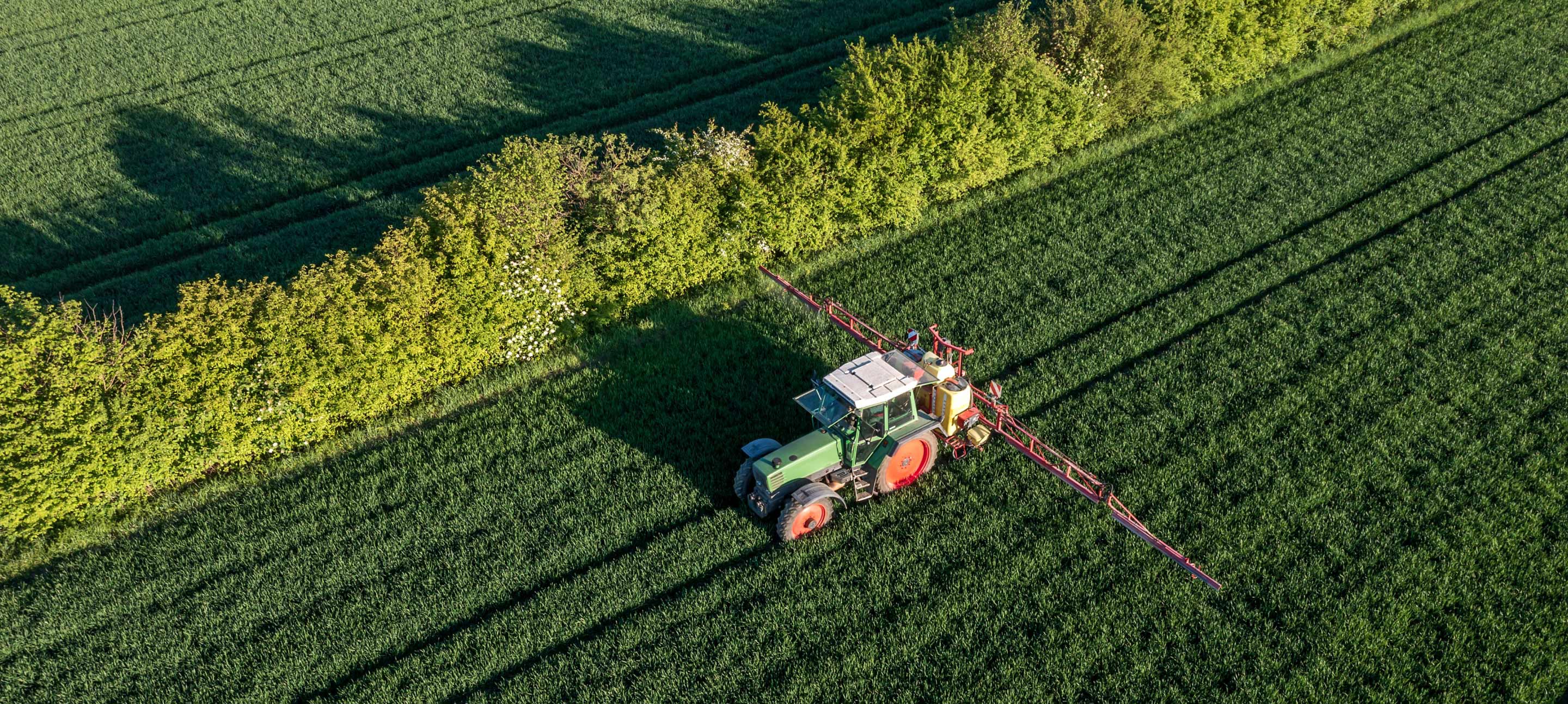 Modern tractor with extended sprayers working on a lush green field, captured from above with clear crop rows