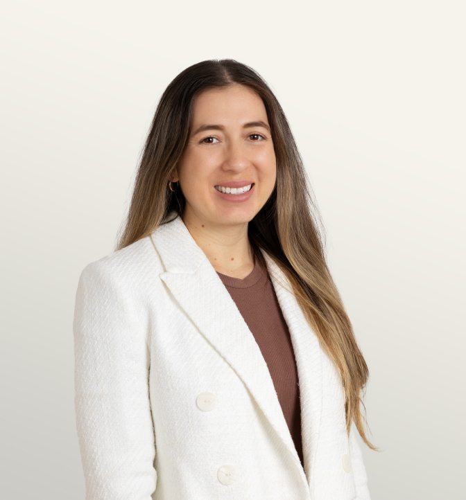 Portrait of a confident woman with long brown hair, wearing a white blazer and a brown top, smiling against a neutral background