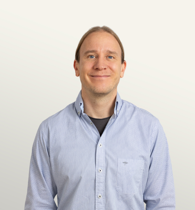 Portrait of a confident man with long blond hair, wearing a light blue button-up shirt, smiling against a neutral background