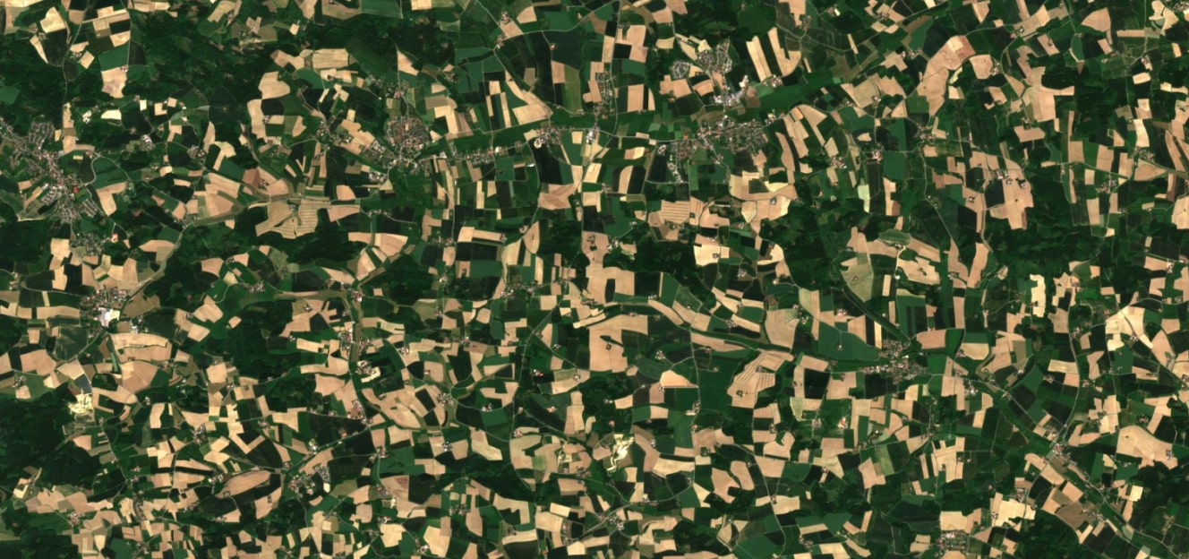 High-resolution satellite image showing a patchwork of green and golden agricultural fields interspersed with small villages and forests