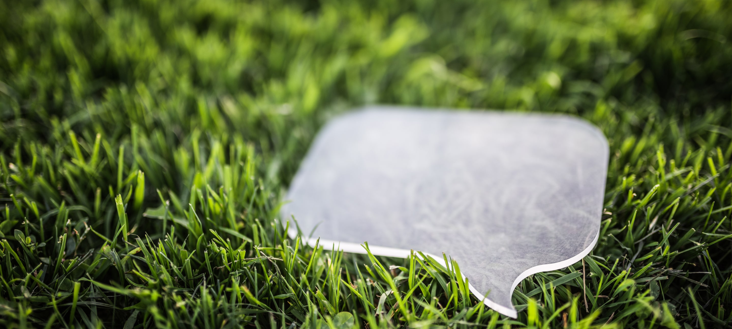 A clear acrylic speech bubble resting on fresh green grass, symbolizing communication and nature