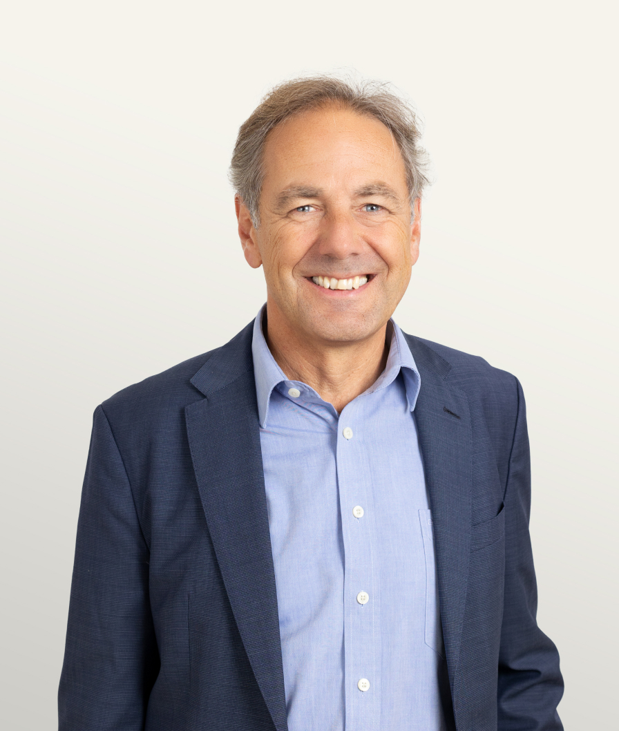 Smiling middle-aged man wearing a navy-blue suit and light blue shirt, posing against a neutral background for a professional headshot.